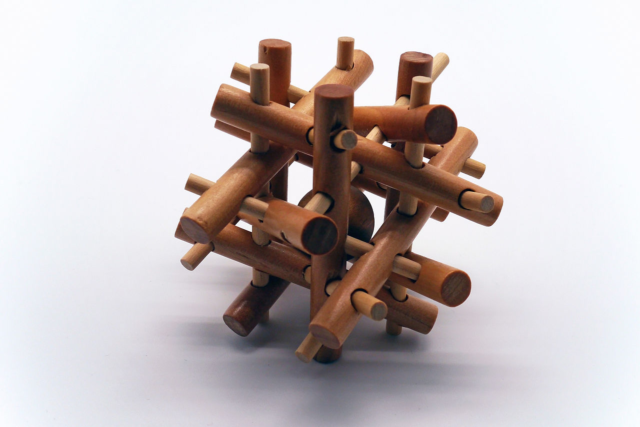 Photo of a solved, wooden tangle puzzle featuring interlocking rods that trap a ball in the center