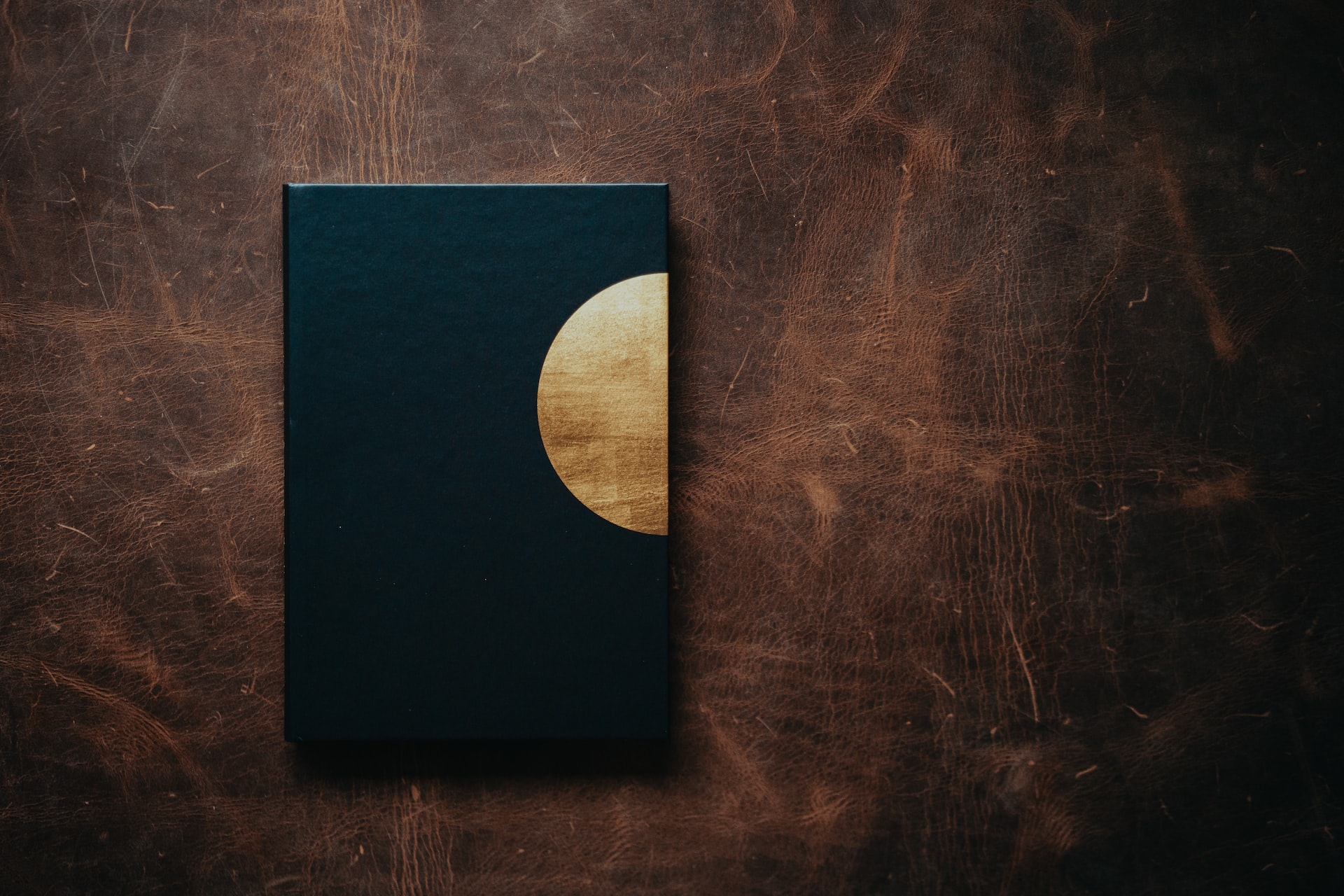 Photo of a black journal with a gold half moon on the cover against a worn brown leather background